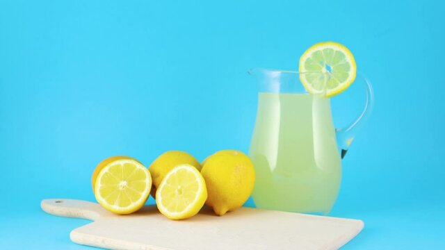 Fresh squeezed lemonade and sliced lemons on cutting board on blue background 