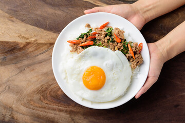 Thai food, stir-fried holy basil with minced pork and fried egg (Pad Kaprao Moo Kai Dao) on plate holding by hand