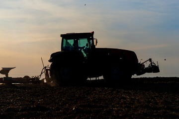Tractor plows the land during harvest at sunset