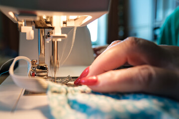 Female hands sew a protective mask using a modern electric sewing machine. Concept of safety during a viral epidemic.