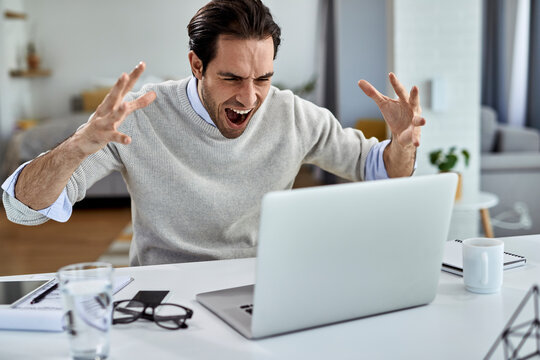 Frustrated businessman screaming while working on a computer at home.