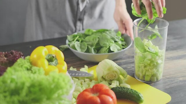 a woman prepares slices on a cutting board ingredients for a celery and spinach smoothie and puts them in a blender bowl