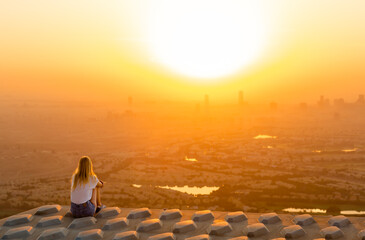Peaceful woman sitting on top of skyscraper overlooking the city during a beautiful sunrise.  