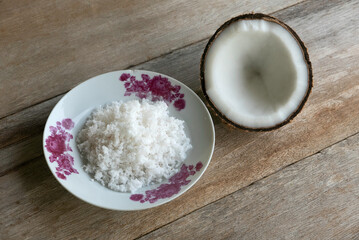Selective focus of coconut and coconut flakes in a plate on a wooden background.