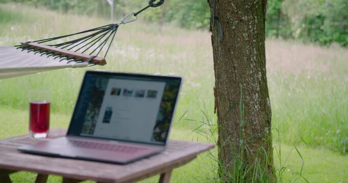 Homeoffice setting with laptop on table in garden next to hammock, pan