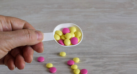 Colored pills scattered on a gray background. Hand holds a spoon with pills. Place for text.