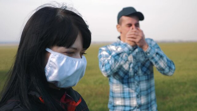 The sick man sneezes. Spread of flu infection in spring or autumn. A woman stands in a cotton mask, protected from the virus.