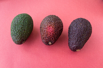 Avocado in different degrees of ripeness on a red background. Flat lay style. Close up. Place for text