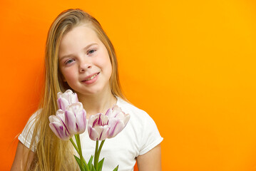 smiling young handsome girl on an orange background with tulips in hands. Children happiness.