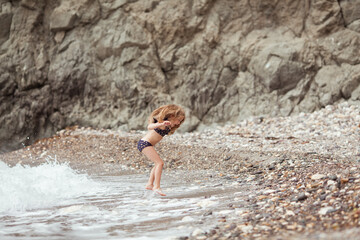 Happy pretty girl walks along the sea coast against the background of the sea, from behind a beautiful landscape