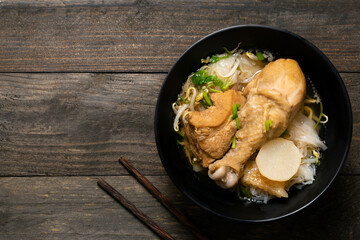 Rice noodle with chicken leg in black bowl on wooden table.