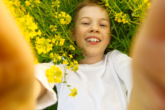 Happy smiling boy making self portrait on smartphone in meadow. young boy making selfie on smartphone laying in green grass with yellow flowers.