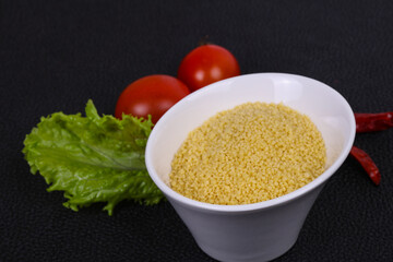 Raw couscous in the bowl served salad leaves, tomato and pepper