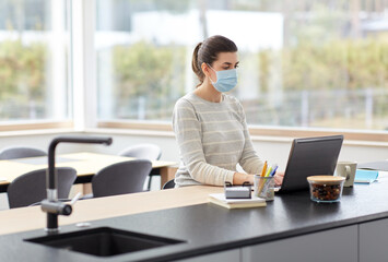 quarantine, remote job and pandemic concept - woman wearing face protective medical mask for protection from virus disease with laptop computer and notebook working at home office
