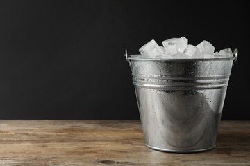 Metal bucket with ice cubes on wooden table. Space for text © New Africa