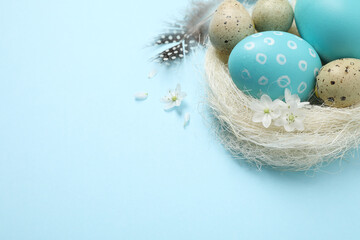 Fototapeta na wymiar Colorful Easter eggs in decorative nest on light blue background. Space for text