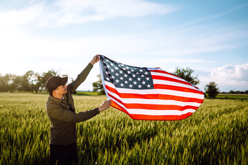 Fourth of July. Patriotic man with the national American flag in the field. Young man proudly waving an American flag. Independence Day. 