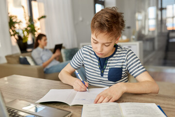 children, education and learning concept - student boy with book writing to notebook at home
