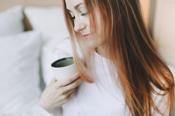 Young beautiful woman with cup of coffee or cacao in bed at home. Girl having breakfast in bed. Morning concept
