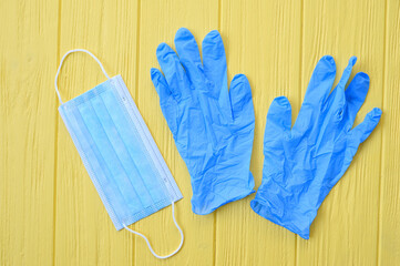 Respiratory face mask and blue gloves on yellow background. Call for hand disinfection. Stop coronavirus concept. Using gloves for hands in shops, during quarantine