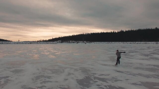Aerial guy Ice skating on a frozen lake, sunset, crazy views. Kelowna, British Columbia, Okanagan, Canada.