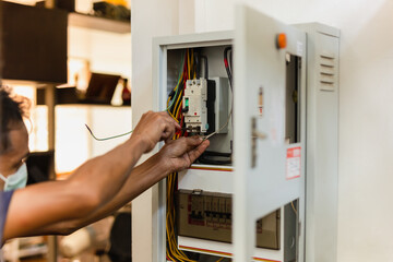 Electrician with medical mask engineer works with electric cable wires of fuse switch box.
