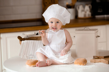 Children's cook. Beautiful, little boy in a white apron and in a cook's hat with a whisk in his...