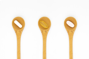 Vitamin supplements on wooden teaspoons against a white background