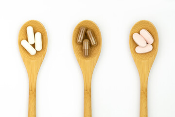 Top view of vitamin supplements on wooden spoons against white background