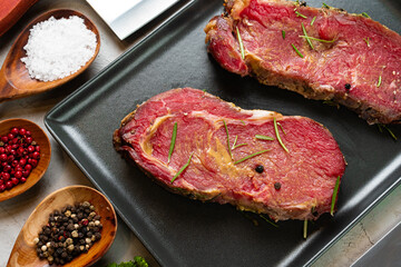 Marinated raw steaks on stone table with spices