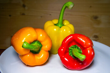 three bellpepers in different colors on plate with wooden background