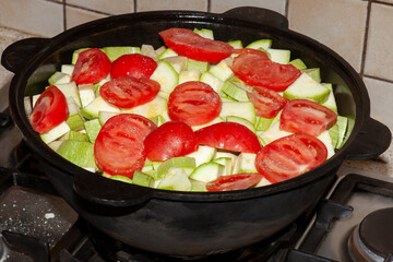 Big cast iron pot, full of vegetables, stewing on stove. Bright red tomatoes and zucchini, vegeterian food, healthy meal concept. Ð¡oarse salt scattered everywhere.
