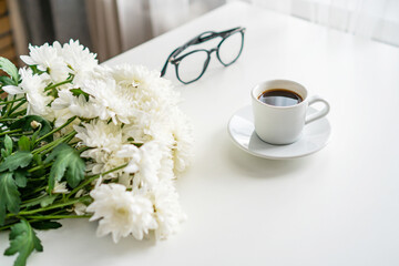 there is a mug of coffee on the table, next to it are glasses and a bouquet of white chrysanthemums