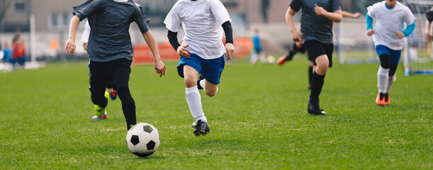 Fototapeta premium Kids Kicking Soccer Ball. Running Soccer Football Players. Four Junior Footballers on Duel. Football Grass Field and Soccer Stadium with Goal in the Background