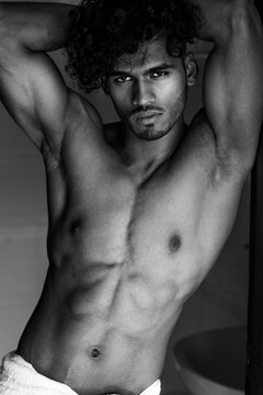 Black and white portrait of an Indian muscled gym fit handsome hunk with a big torso and chest, and big arms with big biceps, and fancy fashionable curly hair