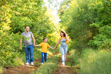 Naklejka na ściany i meble Cheerful parents with son run smiling outdoors in summer evening