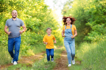 Cheerful parents with son in casual wear smiling run on nature on a summer evening