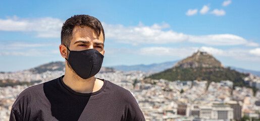 Athens Acropolis, Greece coronavirus days. Young man wearing protective face mask on cityscape and blue sky background.