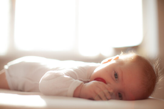Infant Laying With Pacifier On Bed In Lights Of A Sun