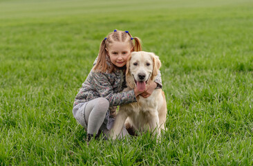 Little girl cuddling dog on field