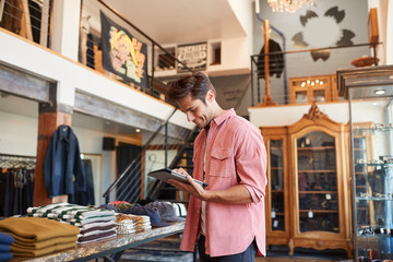 Male Owner Of Fashion Store Using Digital Tablet To Check Stock In Clothing Store