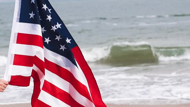Woman hands holding a USA flag in the beach on the background of sea waves
