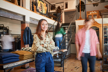 Portrait Of Female Owner Of Fashion Store Standing In Front Of Clothing Display With Customers