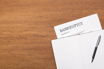 top view of bankruptcy paper and blank notebook with pen on wooden background