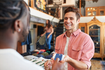 Man In Clothing Store Making Contactless Payment At Sales Desk Holding Credit Card To Reader