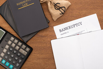 top view of bankruptcy paper, law book, money bag and calculator on wooden background