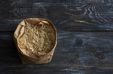 Raw brown long-grain rice in a paper craft bag on a wooden background, space	