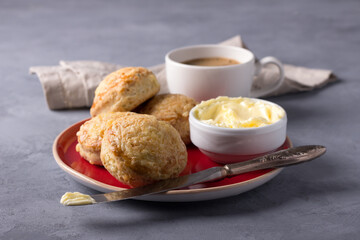 Homemade freshly baked scones with cheese and herbs on a red plate with butter on a gray textured background. Traditional english buns