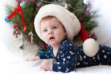 infant in santa hat near christmas tree new year
