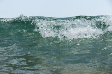 Close up view of sea wave with foam and blue sky at background